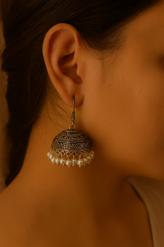 Close-up of a person wearing an ornate silver earring with pearls.