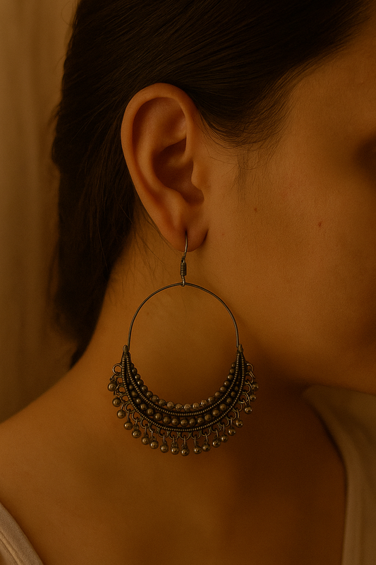 Close-up of an ear wearing a large, ornate hoop earring with a blurred background.